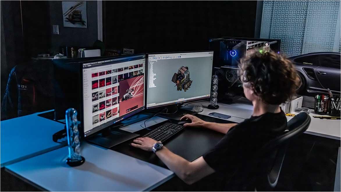 Person using dual monitors with 3D automotive design and concept images on screen.