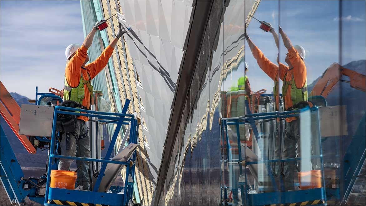 Worker installing wall panels on a lift with glass reflection.