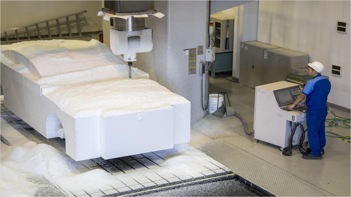 Workers milling a full-sized foam prototype of a car chassis using a CNC machine