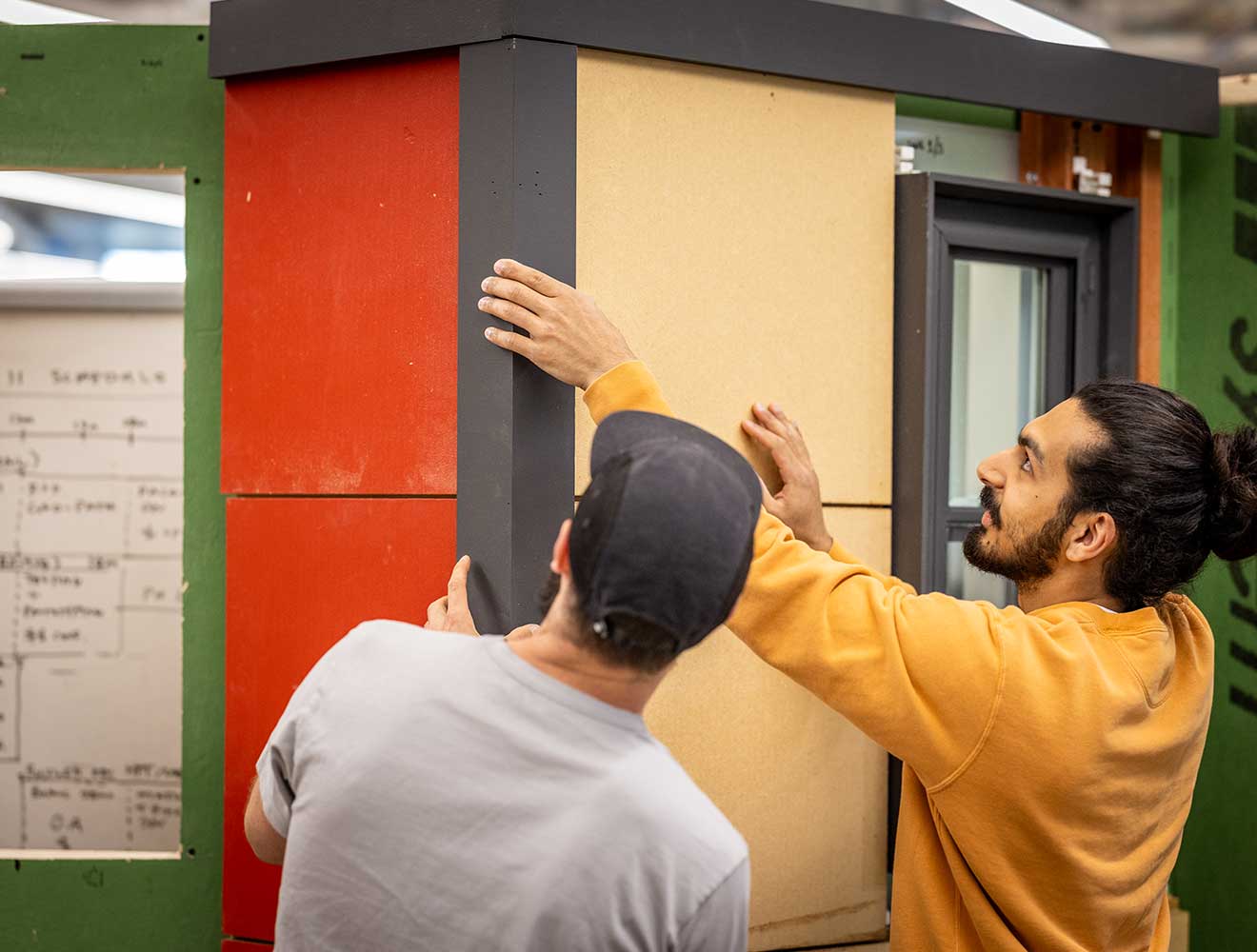 Two men installing wall panels on a building model.
