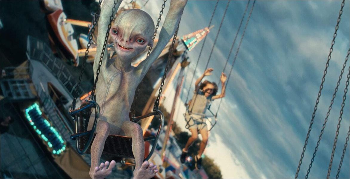 Person on a swing ride at an amusement park with another rider in the background under a cloudy sky.