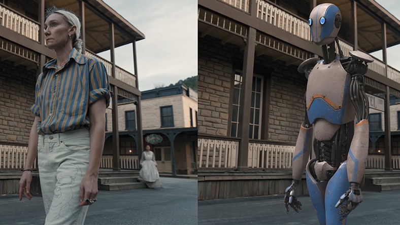 Side-by-side view of a person and a humanoid robot standing on a street in front of old-style wooden buildings.