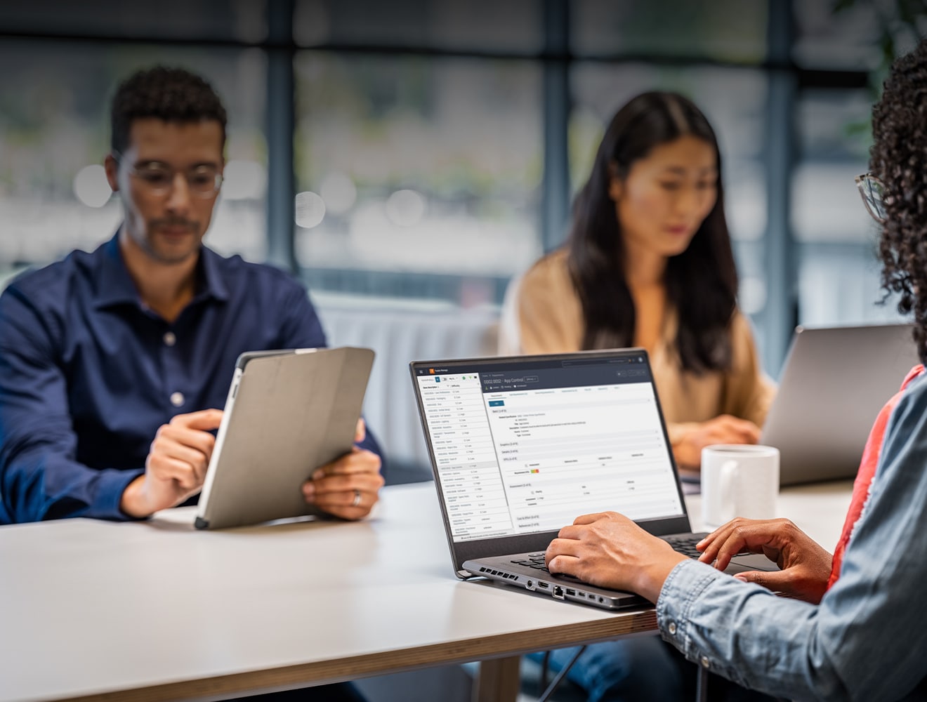 Three individuals seated at a table, each using a laptop, engaged in a collaborative work session.
