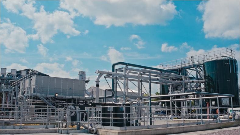 A large industrial plant featuring extensive networks of pipes and machinery against a clear blue sky.