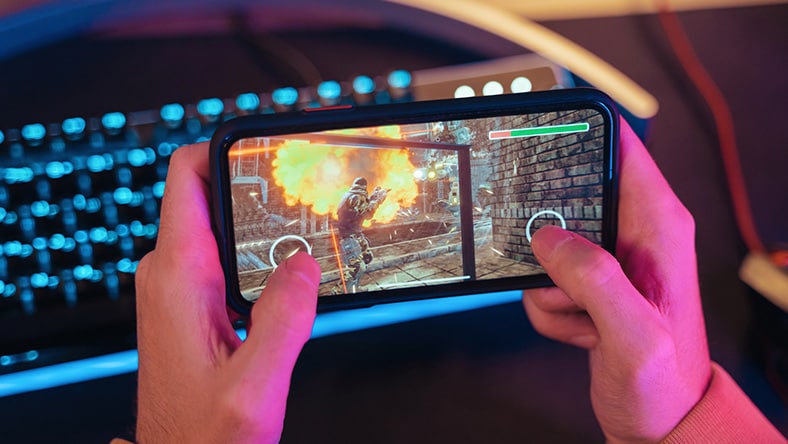 Person holding a smartphone horizontally while playing a first-person shooter video game