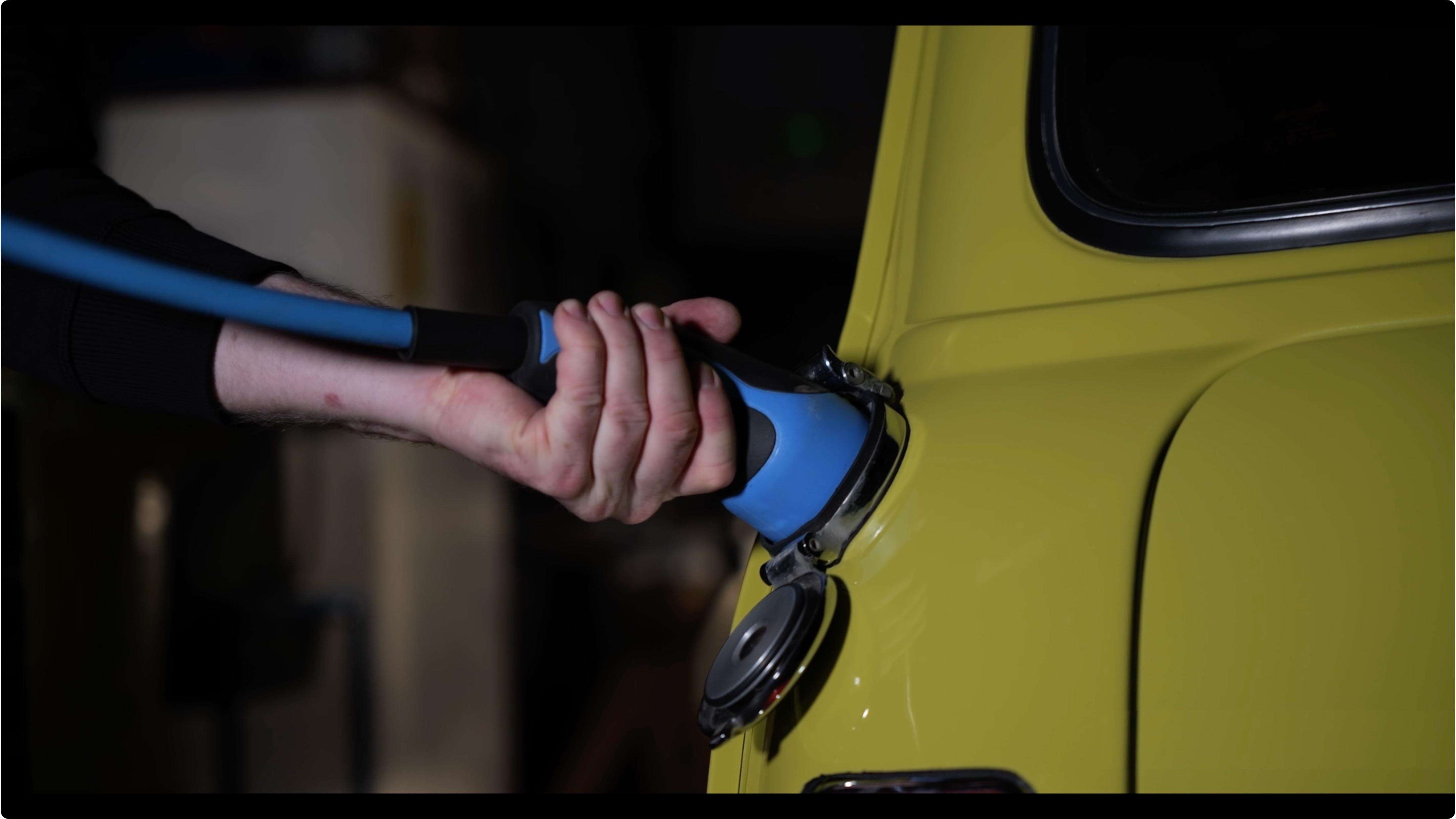 A person's hand plugging a modern electric charge cable into a vintage automobile