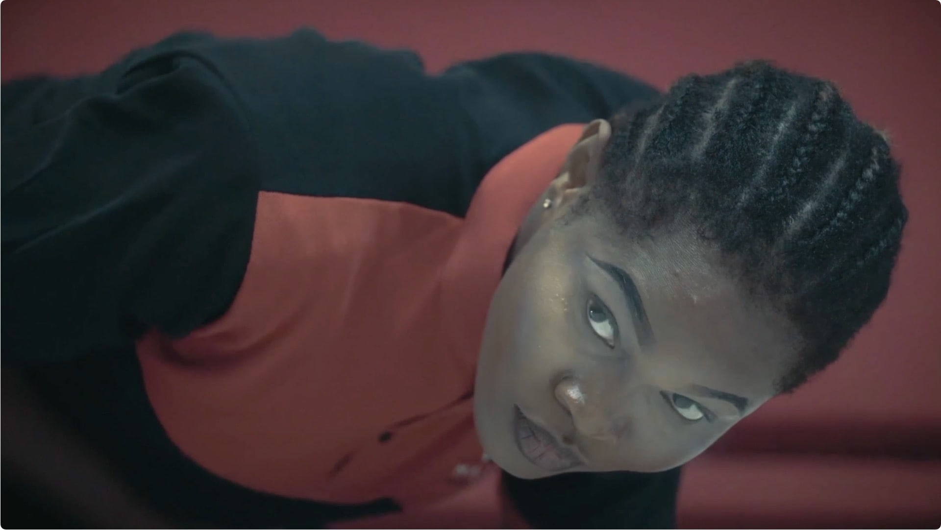 Young woman with cornrow braids in a superhero uniform crouched in a ready position