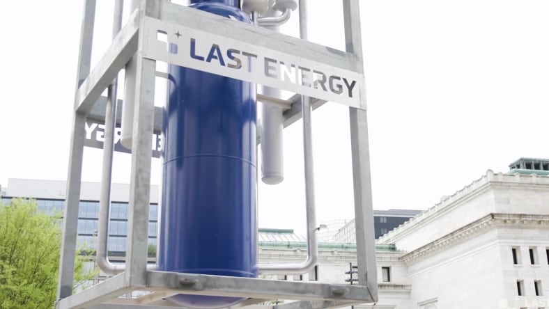 Large metal frame containing prototype power generation components with city buildings in the background