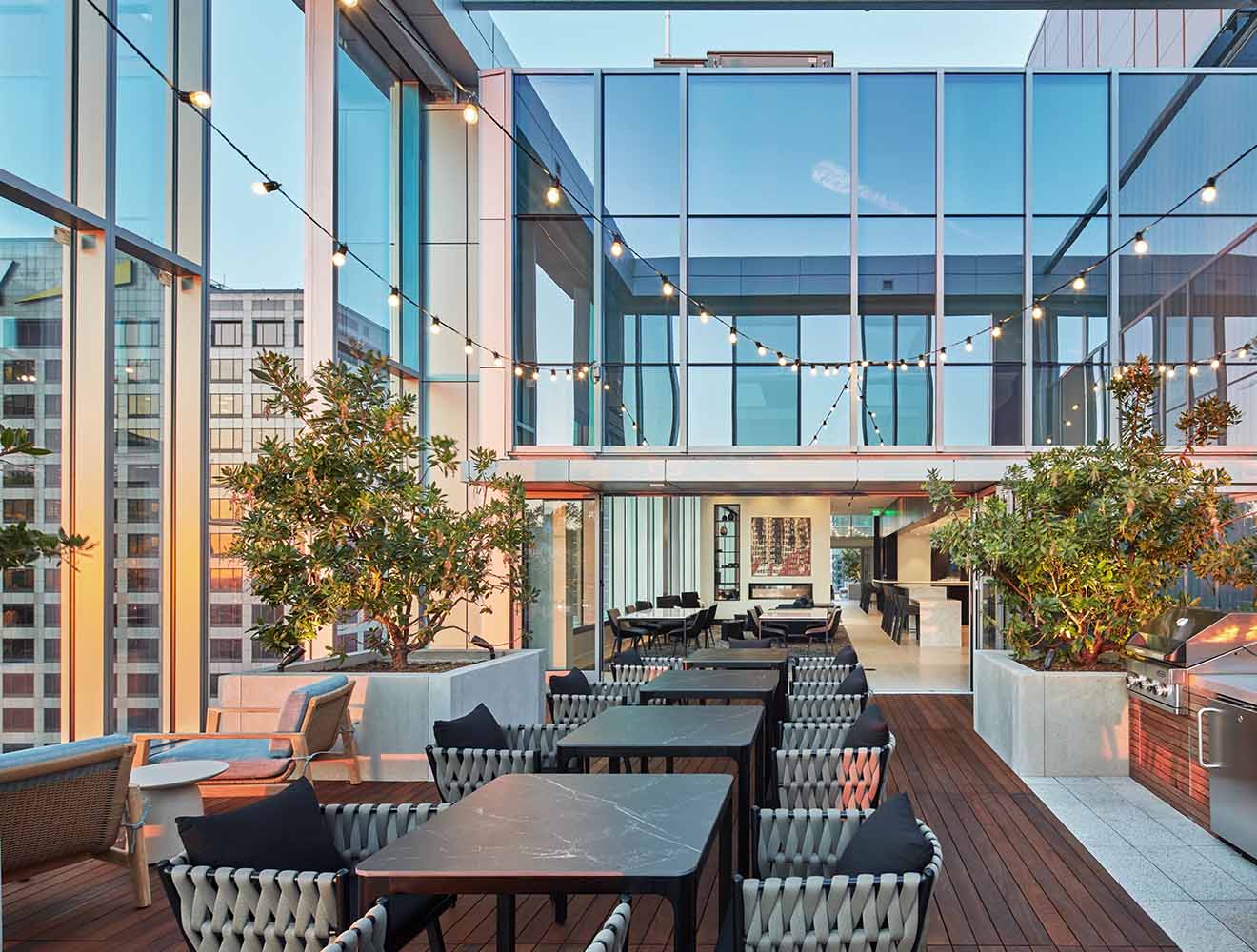Modern rooftop dining area with glass architecture and string lights.