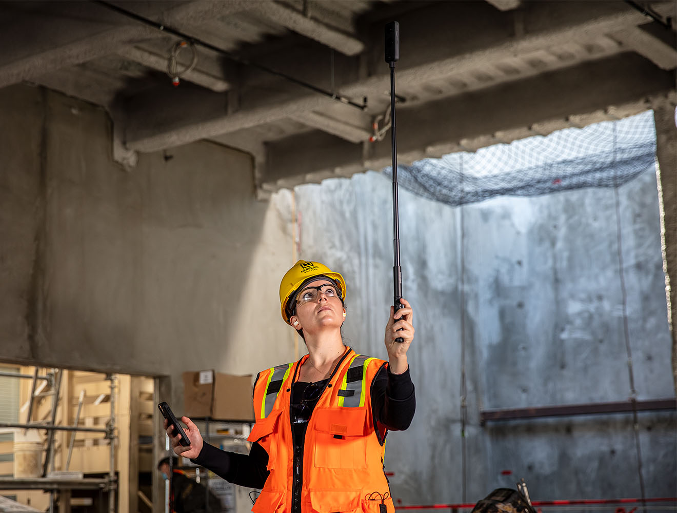 Construction worker inspecting ceiling with a handheld measurement device.