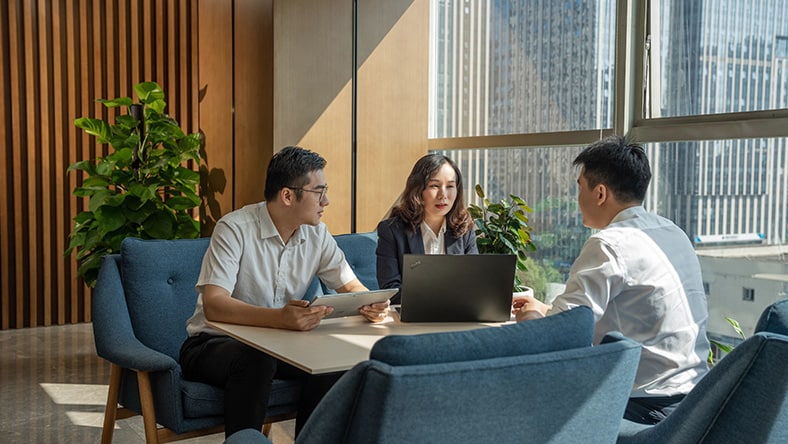 Business meeting with three professionals discussing work at a modern office table.