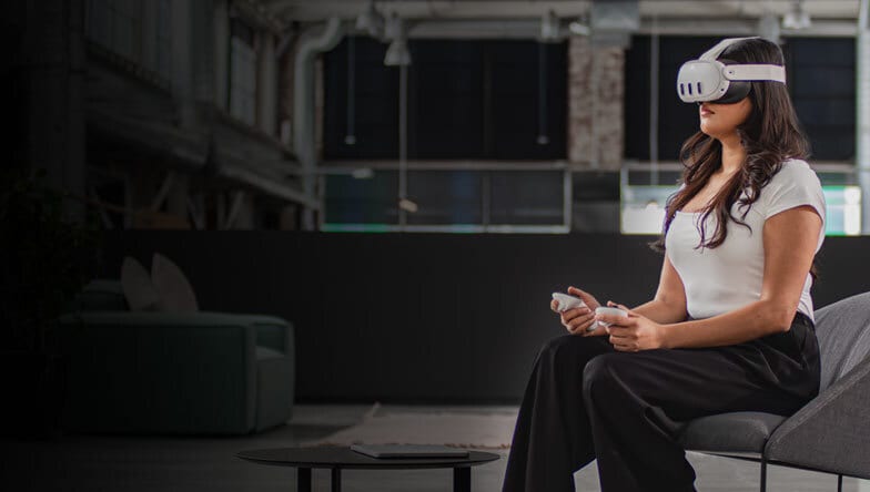 Image of one individual with a VR headset standing and another on his computer 