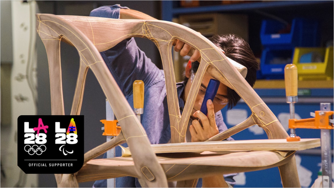 A student works on a wooden chair model in a classroom.