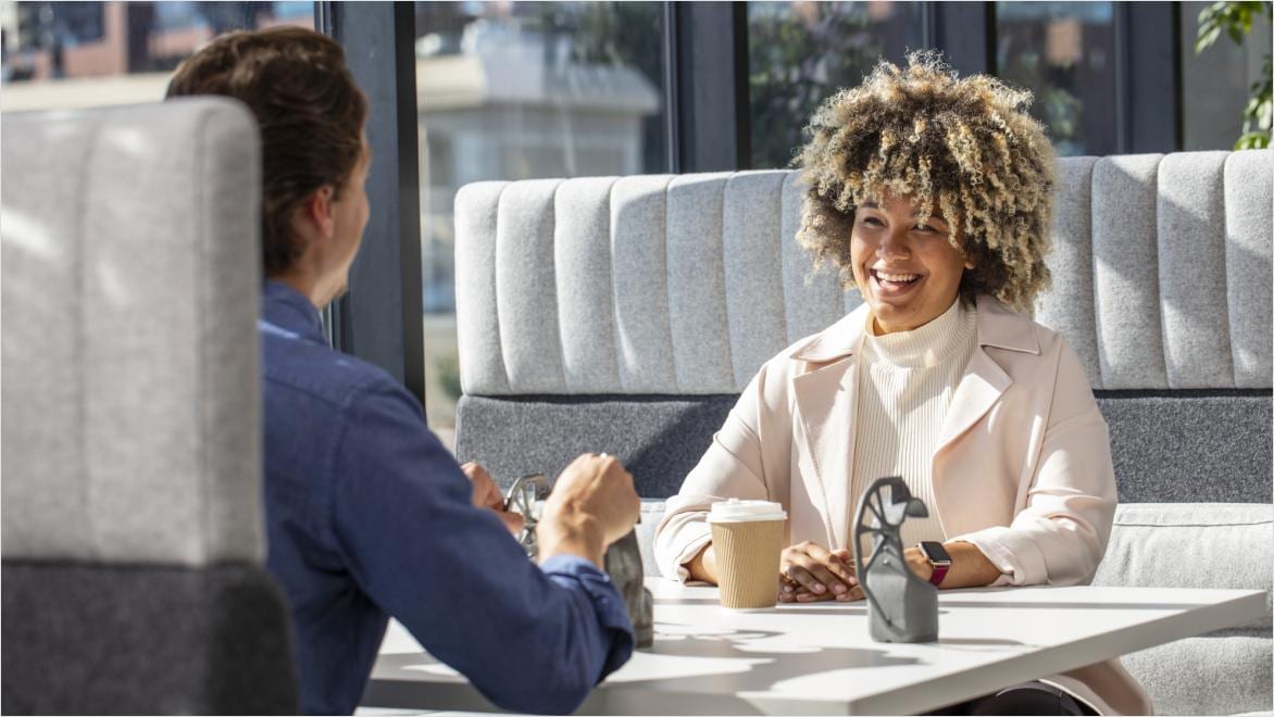Two employees seated at a table in conversation in a casual office lounge setting