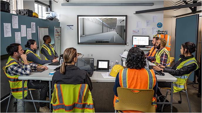 Construction team reviewing Autodesk AI project plans on screen in site office..