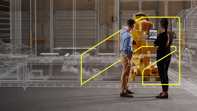 A man and a woman stand in front of a piece of factory machinery. He points at it. Next to the machinery, there's a digital representation of factory machinery.