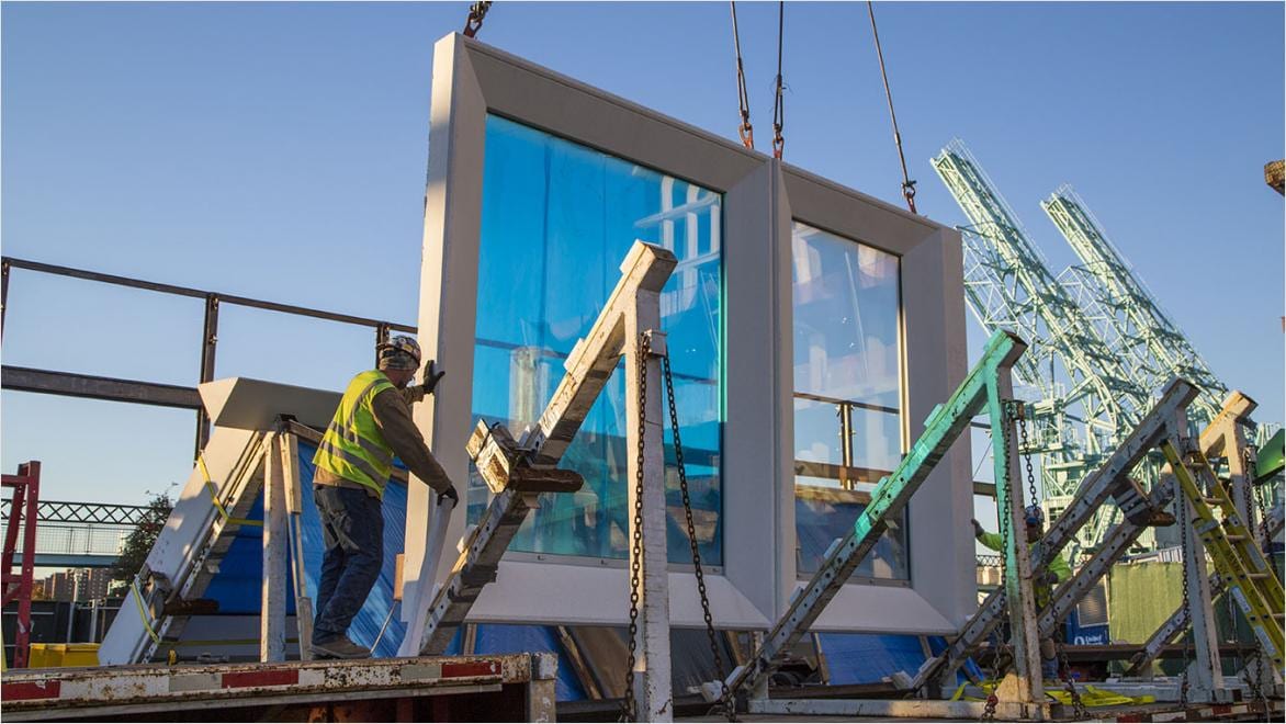 Construction crew guides prefabricated wall panels into place at an industrialized construction site.