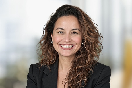 Smiling woman with curly hair wearing a dark blazer against a blurred background