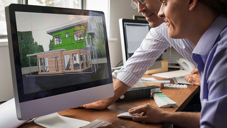 Two designers work on a building rendering on a computer screen.