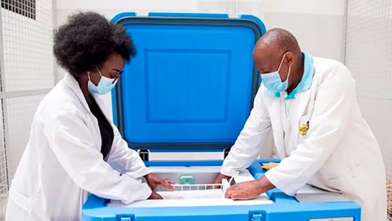 Two medical professionals wearing white scrubs, reaching into a large blue cooler to retrieve Nexleaf ColdTrace devices.