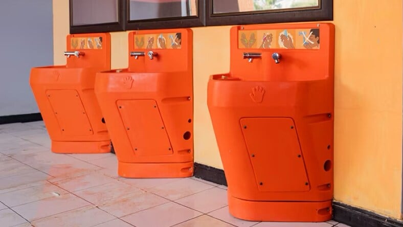 Side view of three orange Splash hand-washing stations installed on an orange wall.