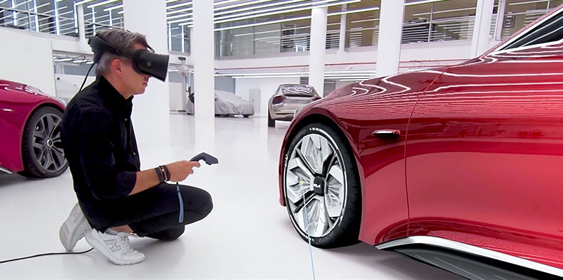 Un dipendente di Kia inginocchiato davanti ad un'automobile rossa indossa un visore VR e tiene in mano uno scanner per i prezzi