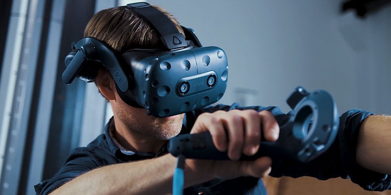 男性のデザイナーが VR ヘッドセットを装着し、右手でジョイスティックを持っている