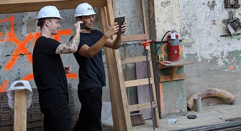 Deux employés de SHoP Architects utilisant une application de réalité augmentée pour superposer un modèle de bâtiment et un chantier dans un environnement industriel extérieur 