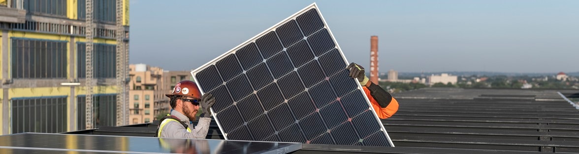 Workers install a solar panel on the roof of a commercial building.