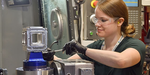 Una donna in un centro tecnologico che rimuove un elemento a 5 assi completo da una macchina CNC Haas VF5SS