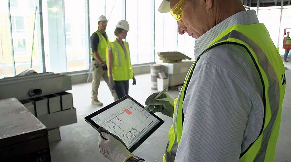 Строительная площадка, на переднем плане человек просматривает планы этажей на планшете