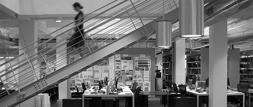 Grayscale photograph of an office with a woman walking down a flight of stairs