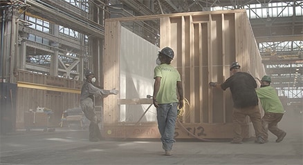 Cuatro hombres trabajando en un edificio modular, en un sitio en construcción polvoriento