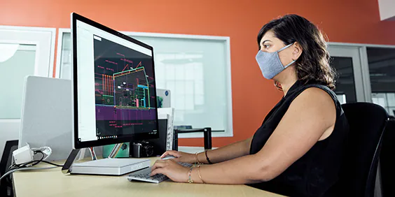 Woman wearing a mask seated at a desk working on a desktop