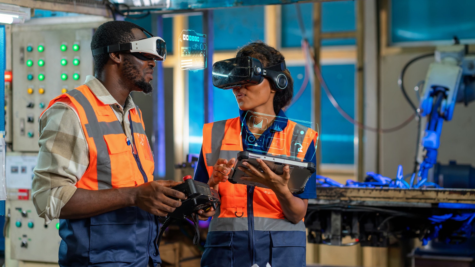 Two people in a factory setting wear AR and VR headsets and hold tablets with digital overlays