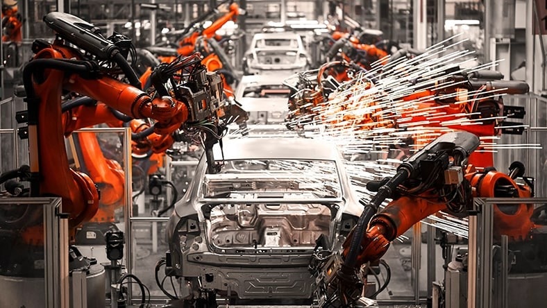 Robotic arms work on car on automotive factory line.