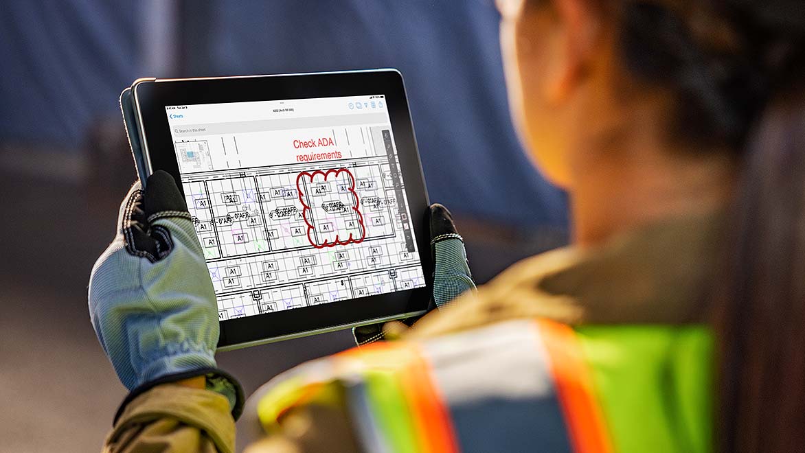 Female engineer in construction clothes reviewing schematic in tablet 