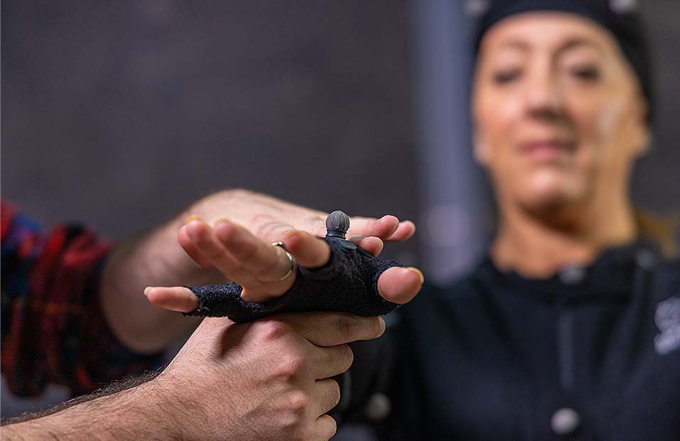 A woman with her hand in a fingerless glove. Her hand is straight out and held up by someone else.