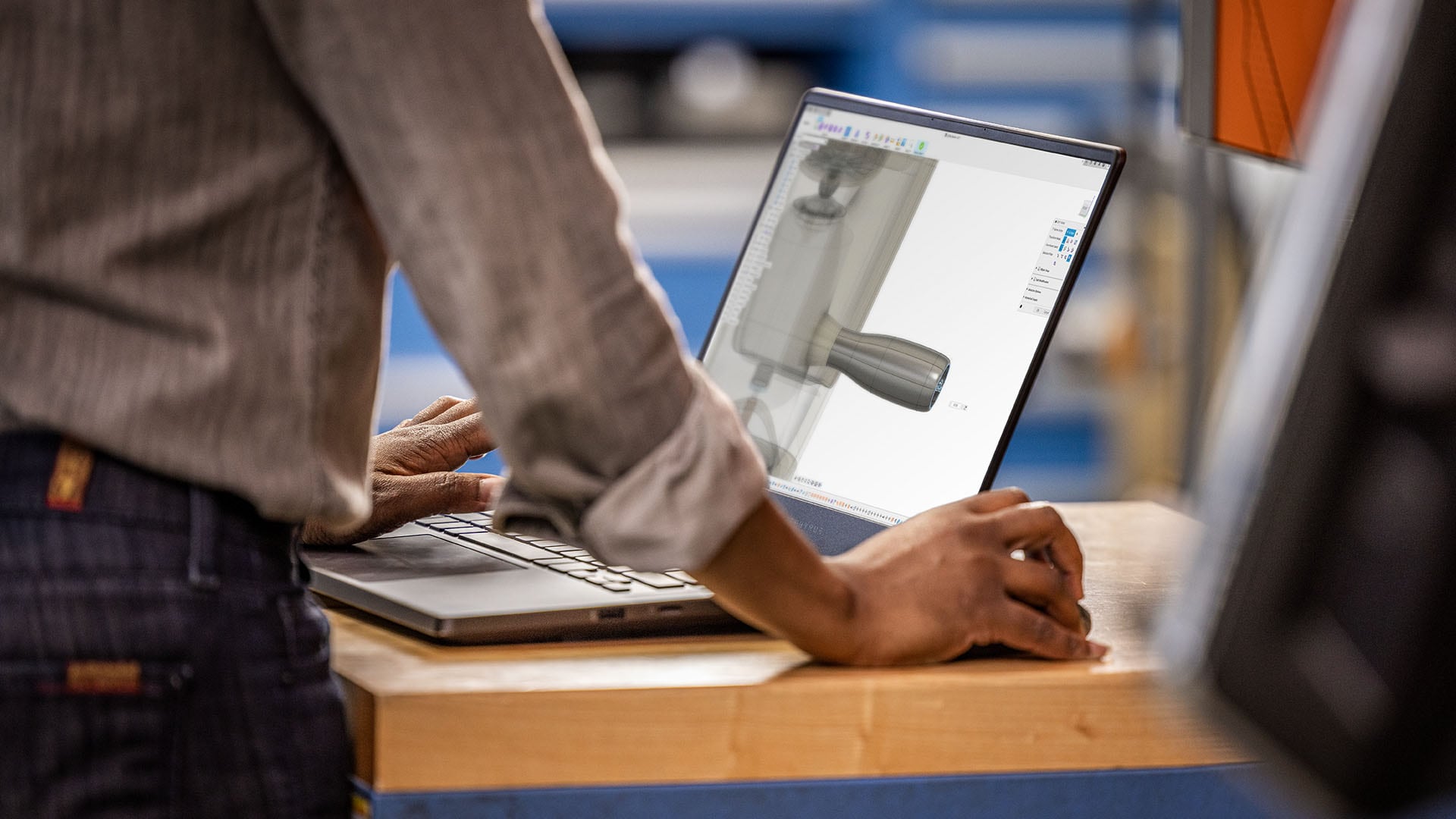 Person stands at desk with open laptop. 