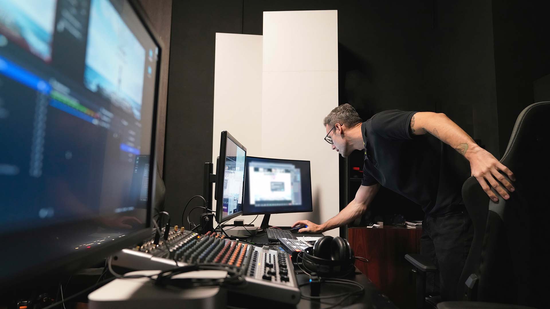 A man leans over a mixing table in a recording studio.