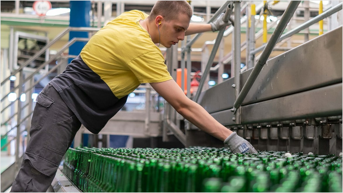 Man leans over array of bottles in a bottling plant. 