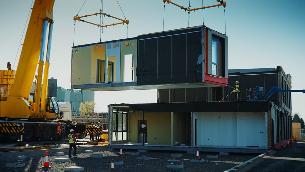 Crane lifts container onto building on a job site. 