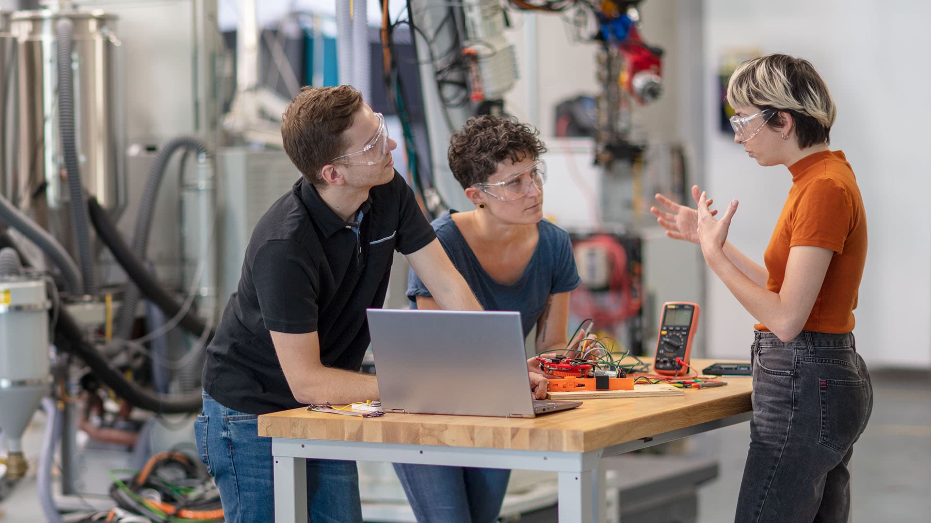 Man and woman stand in front of open laptop in an industrial setting. 