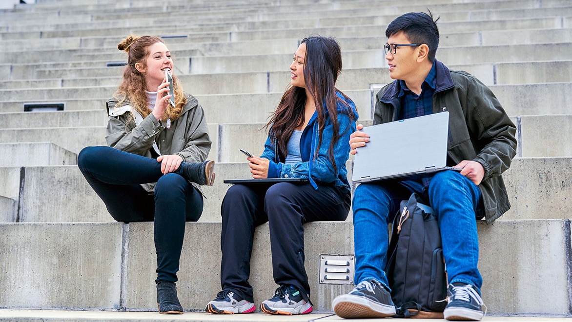 Students sit chatting outside holding laptops