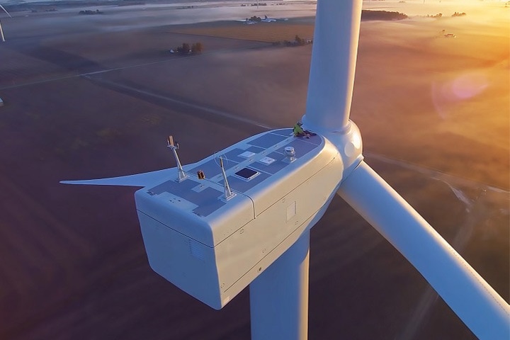 Aerial view of a wind farm showing a worker on top of a giant wind turbine