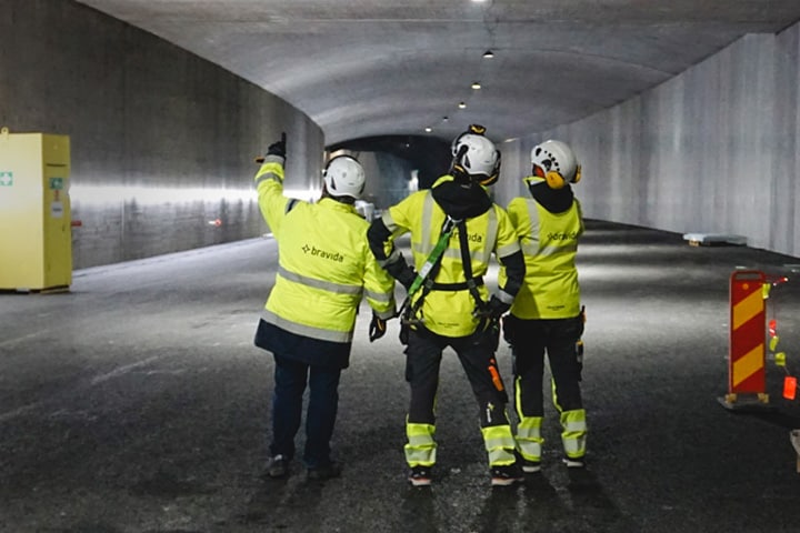 Three construction workers look up at a lighting installation in a highway tunnel