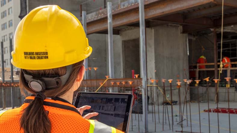 Worker on a construction site reviews a building design on a tablet.