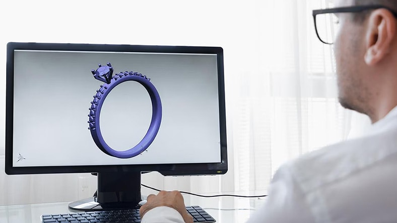 Computer monitor displaying a 3D CAD model of a ring with gemstone, viewed from a side angle.