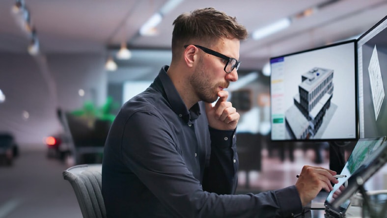 Man at a desk reviewing a 3D building model on monitors during the Autodesk Design & Make Virtual Summit keynote
