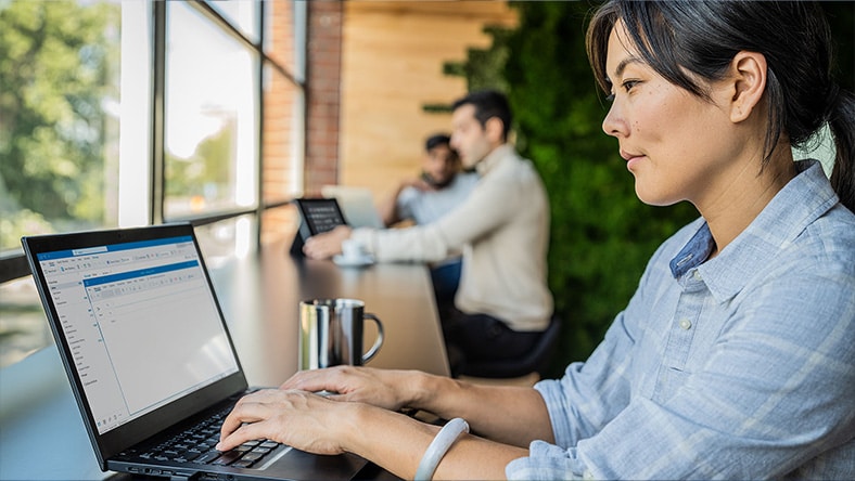 Woman working on a laptop in a bright office with colleagues behind her, discussing practical AI and connected data